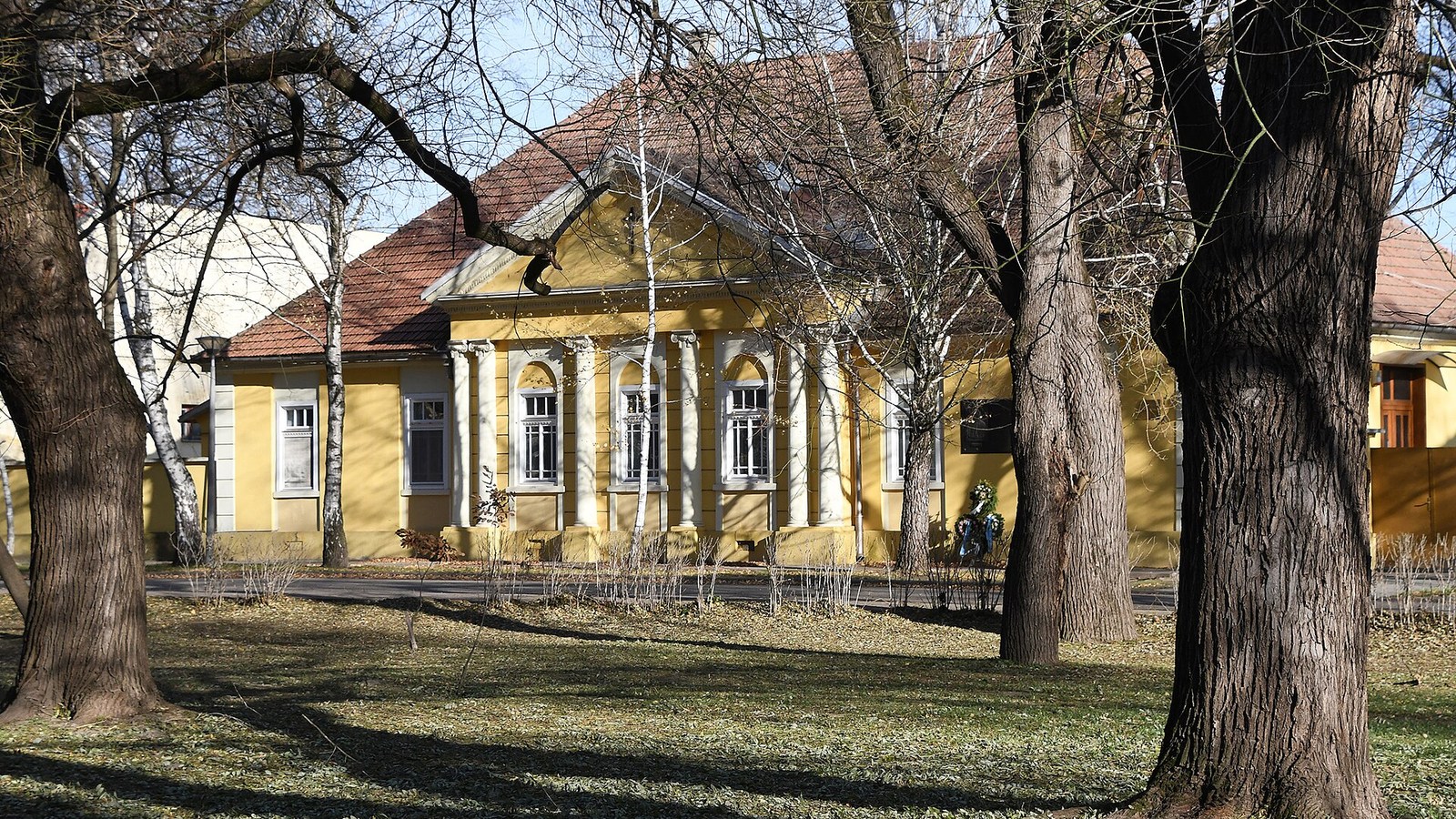 Bácsalmás, az egykori római katolikus plébánia épülete a Hősök terén, a park lombtalan fái között.