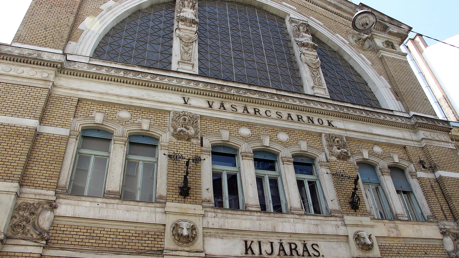 Budapest, a Hold utcai piac sárga téglás, szobrokkal díszített csarnokhomlokzata a nagy, félköríves üvegablakkal.