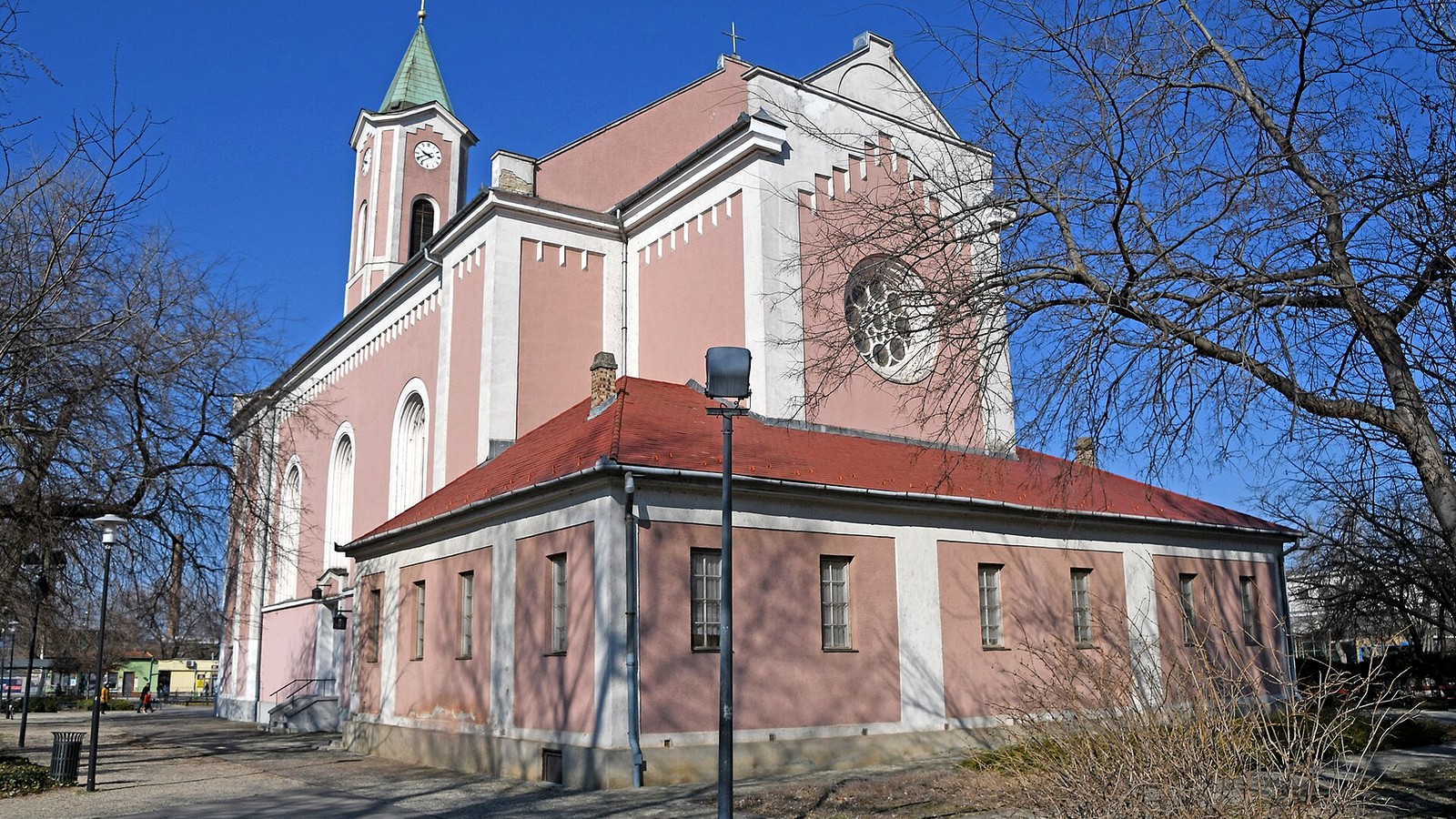 Csepel, a Szent Imre téri római katolikus templom rózsaszín, tornyos homlokzata kék ég alatt.