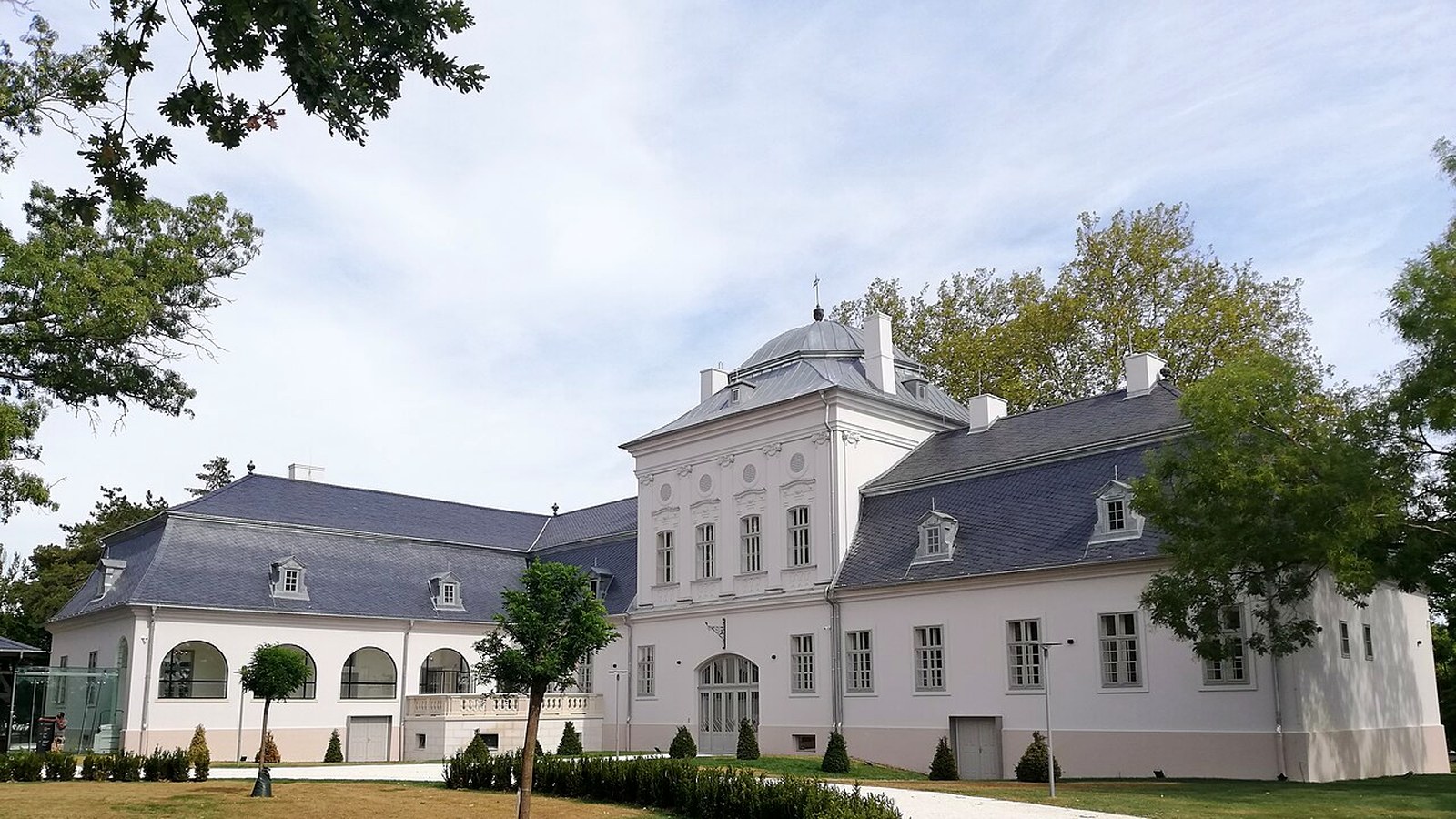 Geszt, a fehér Tisza-kastély szürke tetővel, előtte nyírt gyep és sétány a parkban.