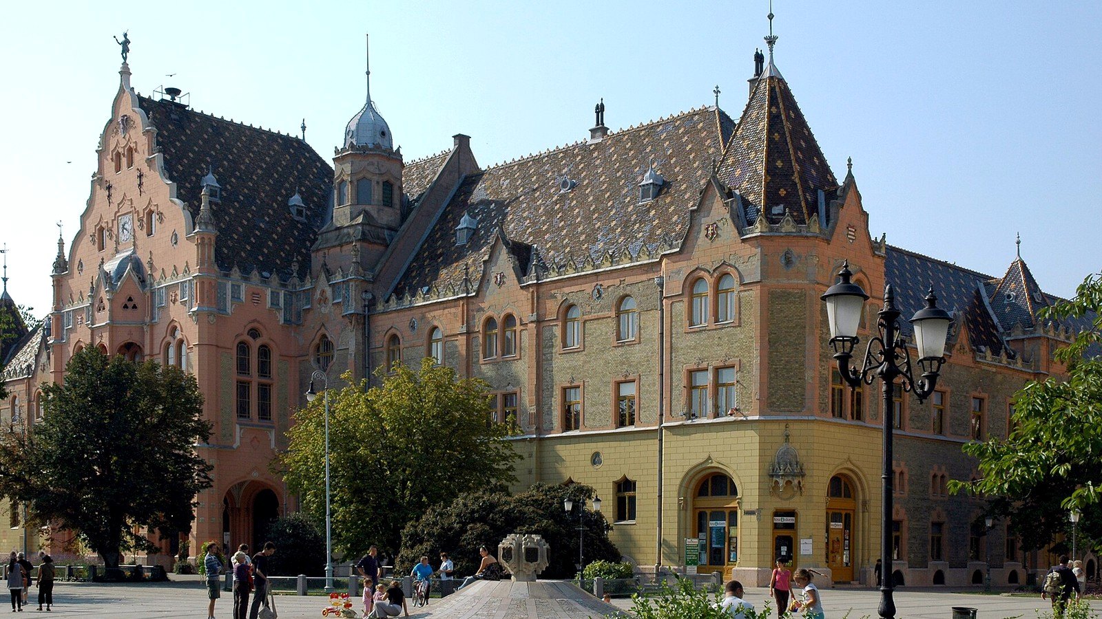 Kecskemét, a Városháza szecessziós homlokzata színes Zsolnay-cserepes tetővel és tornyokkal a Kossuth téren, előtte sétálókkal.