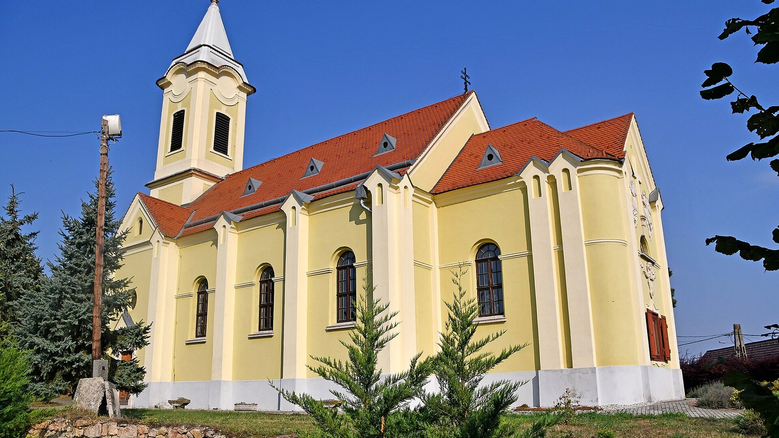 Kocs, a katolikus templom sárga fala, piros teteje és karcsú tornya mélykék ég alatt.