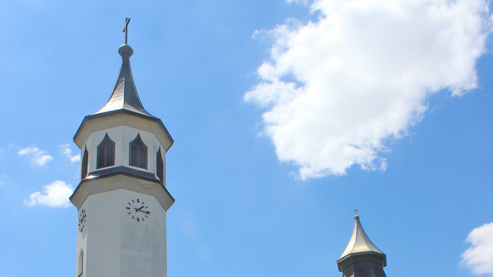 Martfű, a Szent Tamás-templom órás harangtornya és csúcsos toronysisakja kék ég előtt.