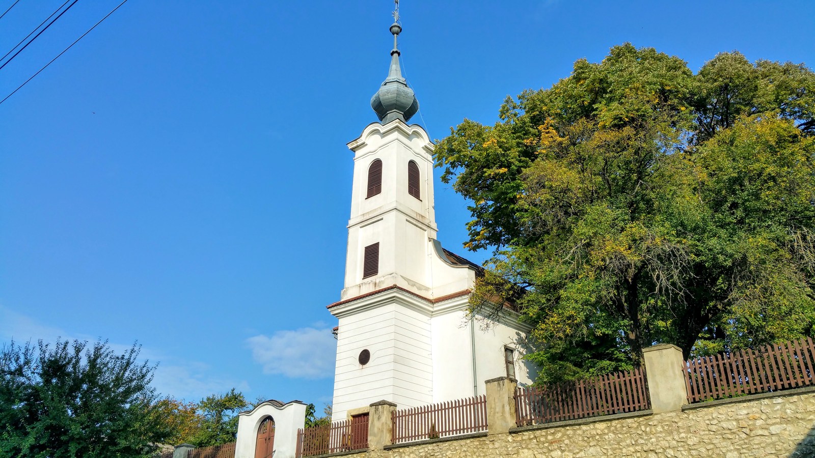 Nagypall, az 1793-ban épült református templom fehér tornya hagymasisakkal, mellette nagy lombos fa, előtte terméskő támfal fakerítéssel.