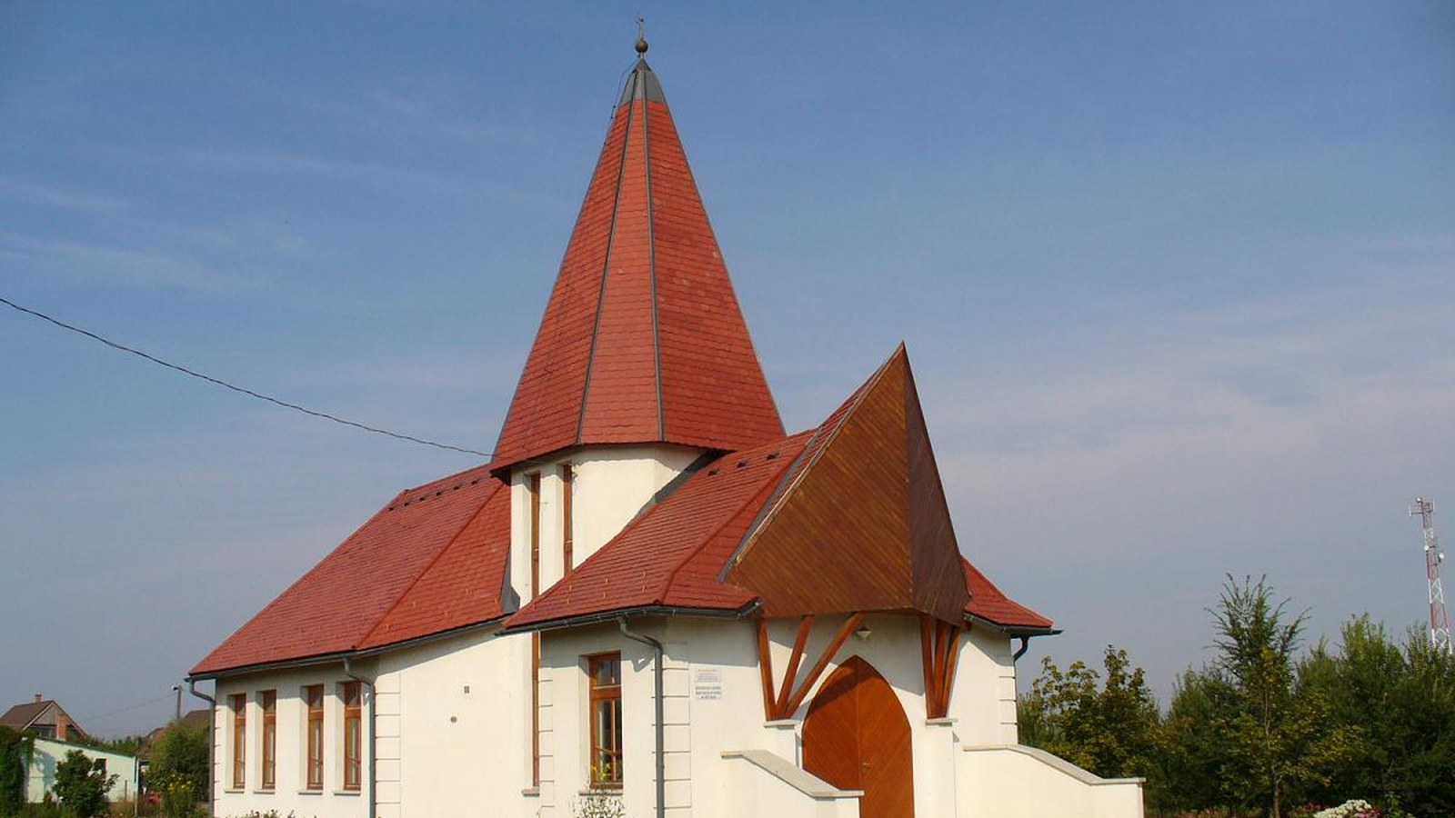 Szajol, a piros tetős, csúcsos tornyú református templom virágos kerttel.