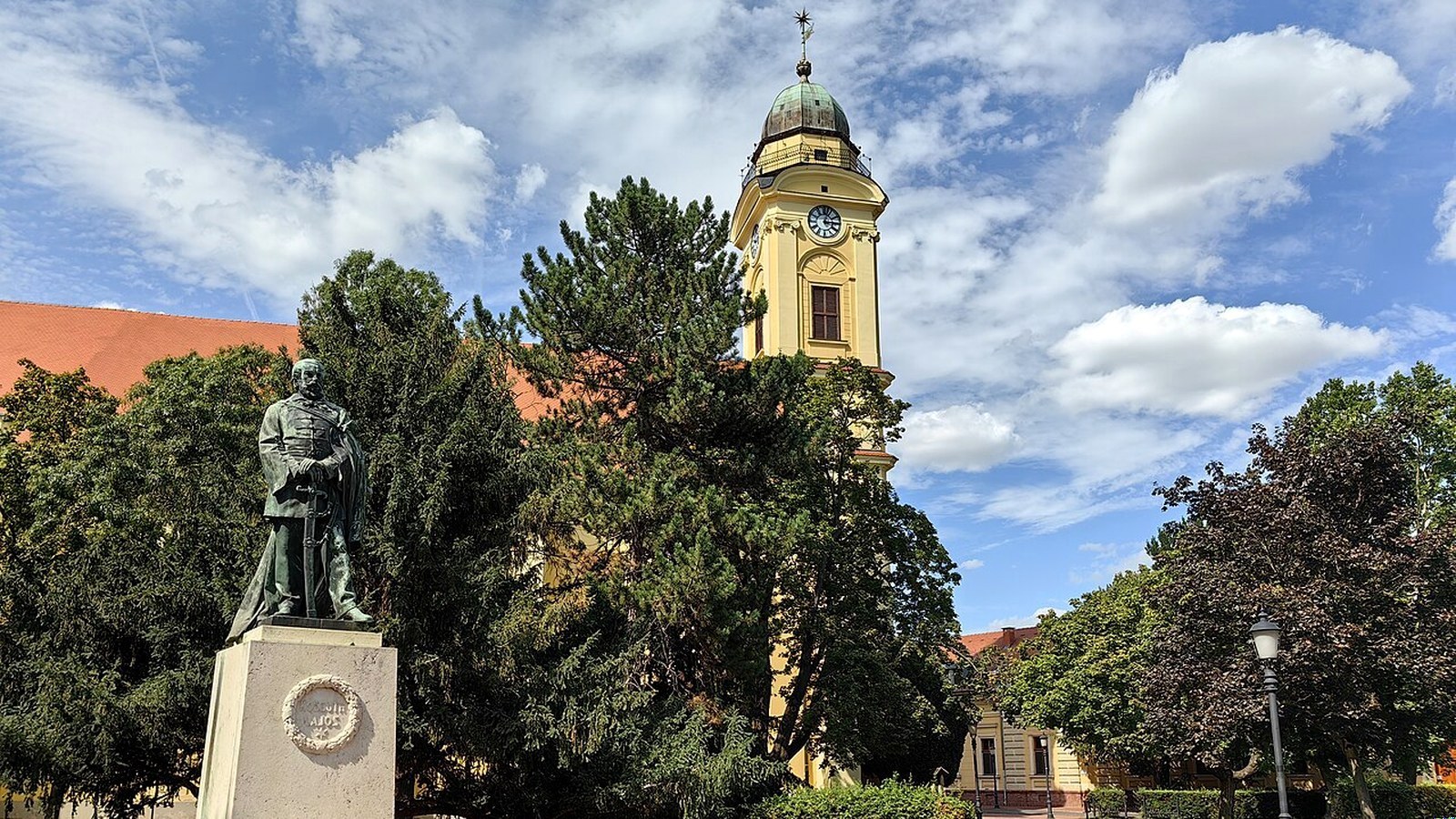 Szentes Kossuth tér szabadtéri látképe Kossuth Lajos szoborral és református templomtoronnyal — szabadon bejárható köztér / park tengely (Széchenyi liget kiegészítés; élménymedence / termál nem 0 Ft).