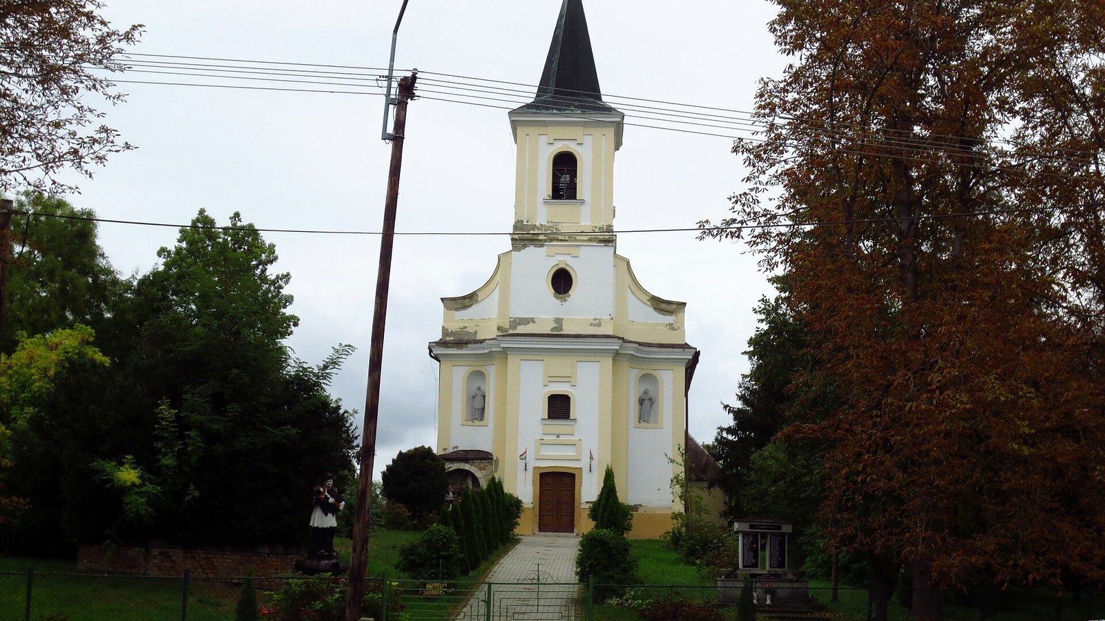 Tarnaméra utcaképe a fehér tornyú római katolikus templommal és őszi fákkal.