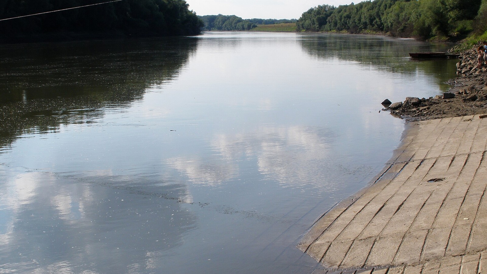 Tiszaroff, a Tisza nyári képe a vízben tükröződő felhőkkel és a burkolt parti lejáróval.